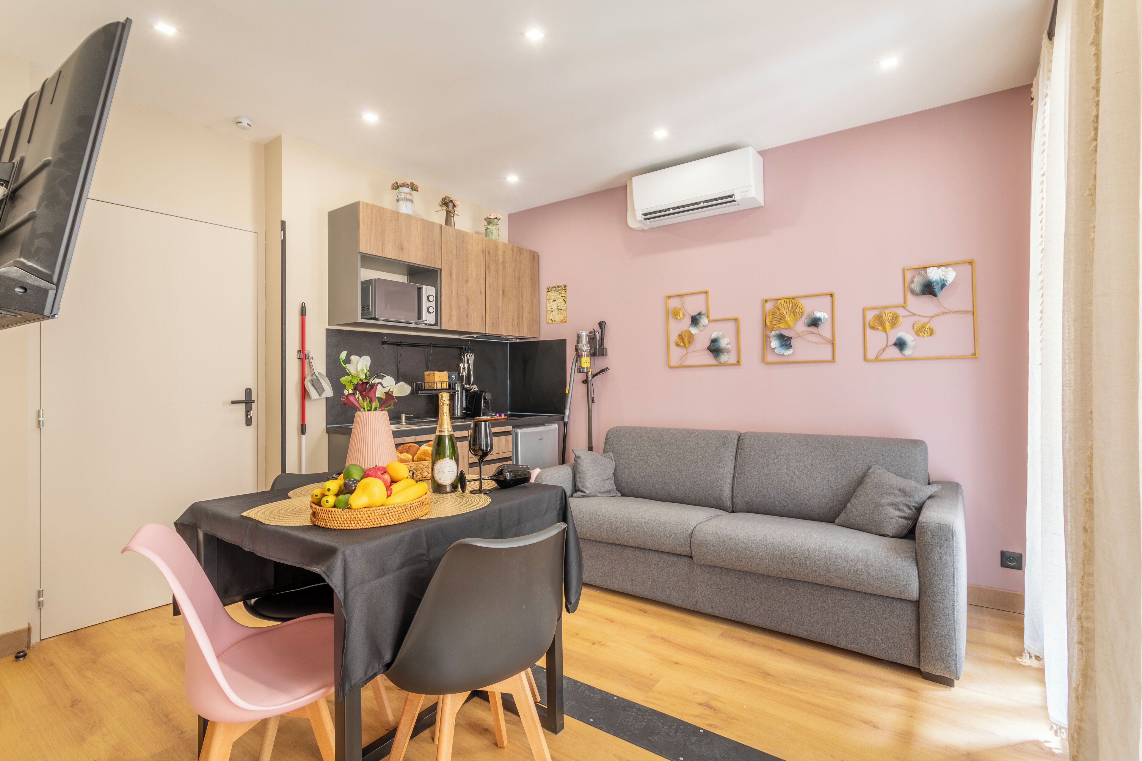 Un espace de vie compact comprenant un coin repas, une kitchenette et un canapé gris.