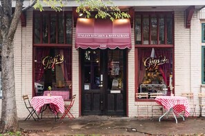 An Italian kitchen and restaurant with a vintage sign, outdoor seating with checkered tablecloths, and a tree in front.