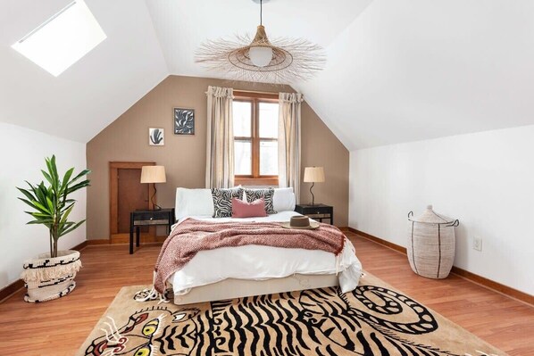 A bedroom with a sloped ceiling, a bed with a zebra-patterned rug, a potted plant, and a hanging light fixture.