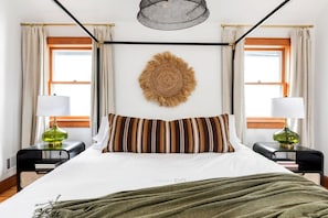 Ein ordentlich gemachtes Bett mit gestreiften Kissen, einer Wanddekoration und zwei Nachttischlampen.