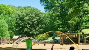A playground with a swing set, slide, and sand area, surrounded by trees. - Espresso Martini (Atlanta)