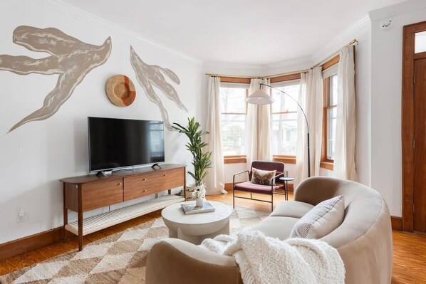 A modern living room with a flat-screen TV, wooden cabinet, round coffee table, beige sofa, and a potted plant.