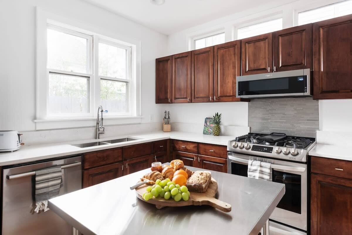 A modern kitchen with wooden cabinets, a stainless steel microwave, and a central island with a fruit platter.