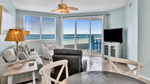 Un salon avec vue sur la plage, un ventilateur de plafond et un téléviseur.