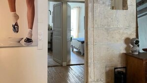 A rustic interior with exposed wooden beams, a hanging light fixture, a mirror, and a doorway leading to another room. - Spacieux 2 Chambres Dans le Centre D'arles Avec Terrasse (Arles)