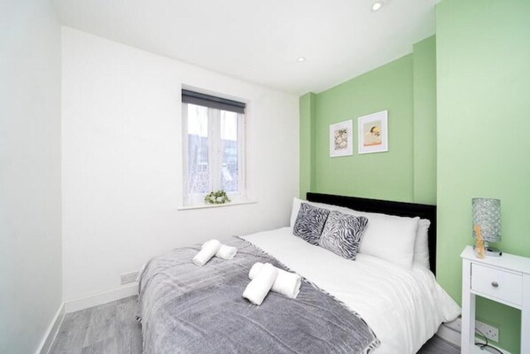 A bedroom with a bed, pillows, a nightstand, a lamp, and a window.