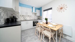Et moderne køkken med hvide skabe, et mønstret backsplash og et spiseområde med et træbord og stole.