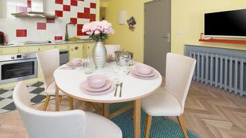 Een eetgedeelte met een ronde tafel voor vier personen, omringd door witte stoelen. Op de tafel staat een vaas met roze bloemen.