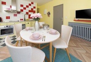 Een eetgedeelte met een ronde tafel voor vier personen, omringd door witte stoelen. Op de tafel staat een vaas met roze bloemen.
