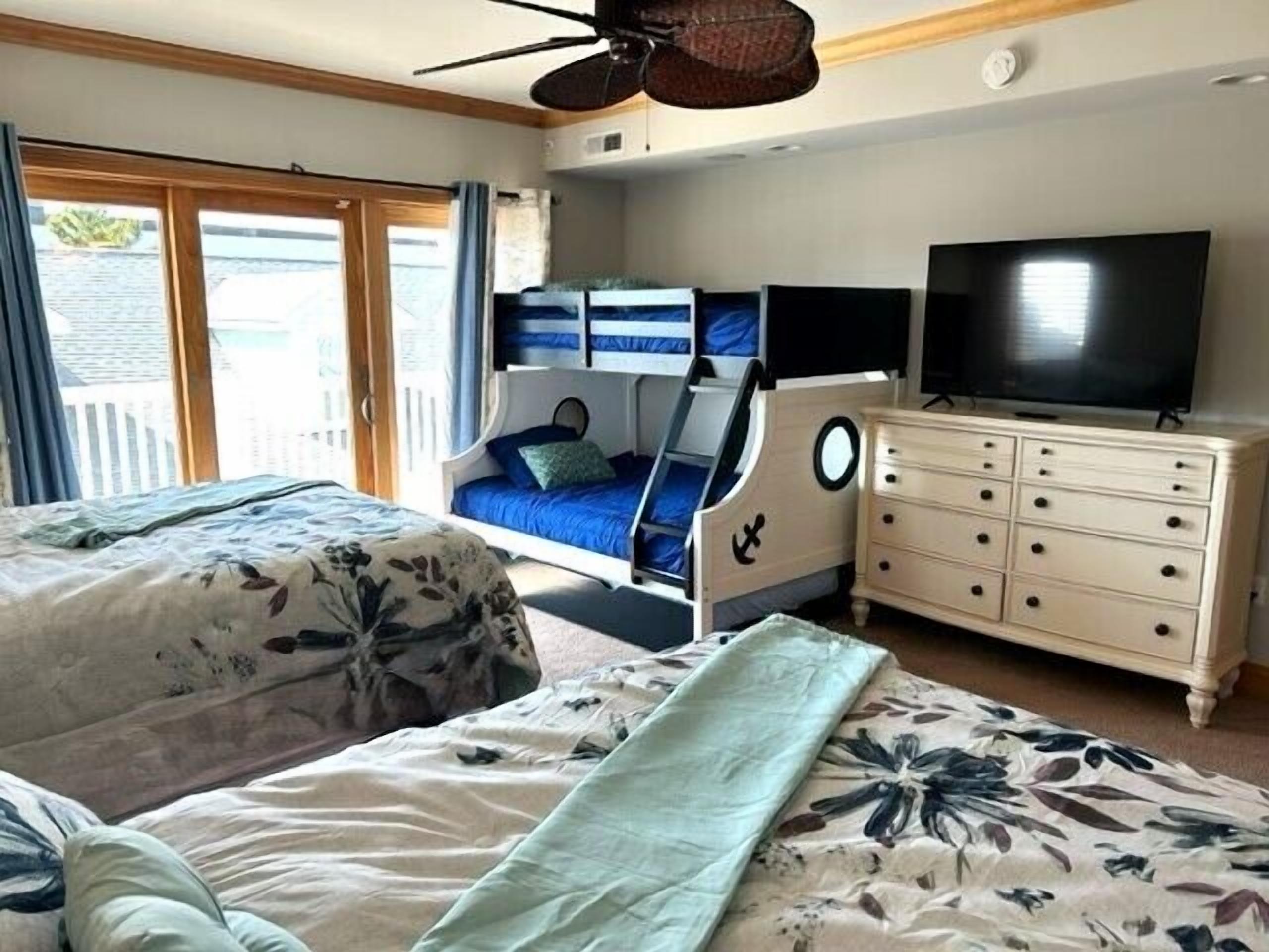 Una camera da letto con due letti, una TV, un comò e una ventola a soffitto.