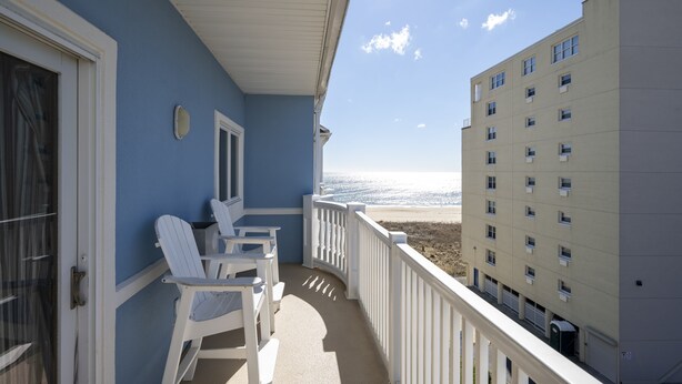 A balcony with white chairs and a view of the beach.