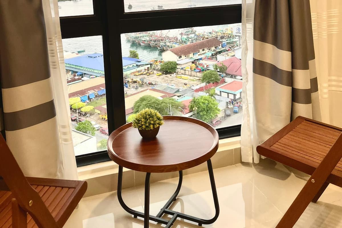 Una habitación con un ventanal grande, una mesita redonda con una planta y dos sillas de madera.