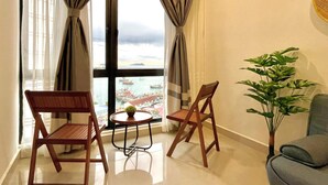 A room with two wooden chairs, a small table with a plant, and a view of a harbor through large windows. - Covesign Suite, The Shore Kota Kinabalu (Kota Kinabalu)