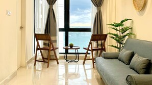 A living room with a large window, two wooden chairs, a small table, and a grey sofa. - Covesign Suite, The Shore Kota Kinabalu (Kota Kinabalu)