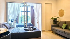 A modern hotel room with a large bed, a sofa, a dining table, and a view of greenery through the windows. - Covesign Suite, The Shore Kota Kinabalu (Kota Kinabalu)
