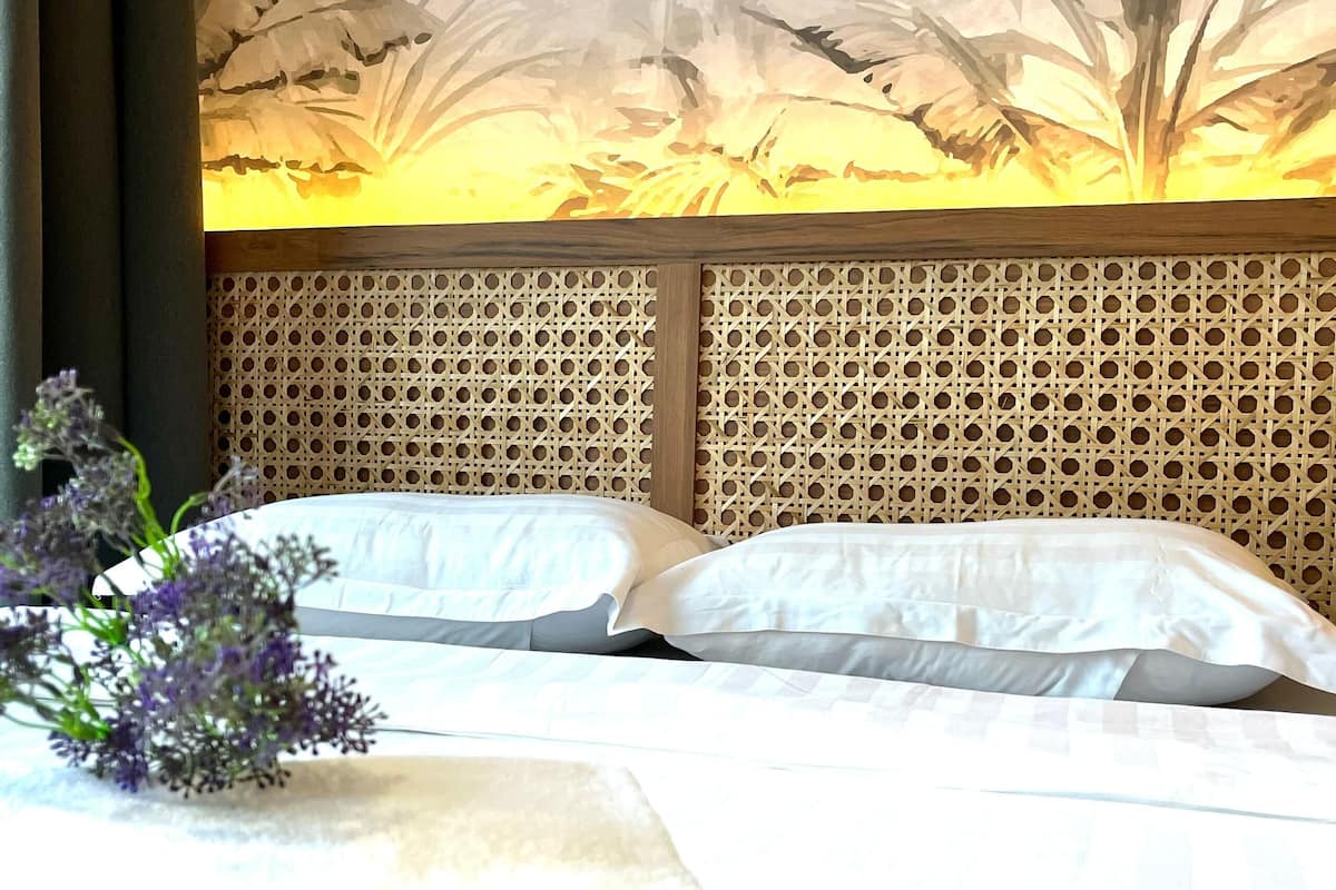 Una habitación de hotel con una cama, ropa de cama blanca, un panel decorativo y un arreglo floral.
