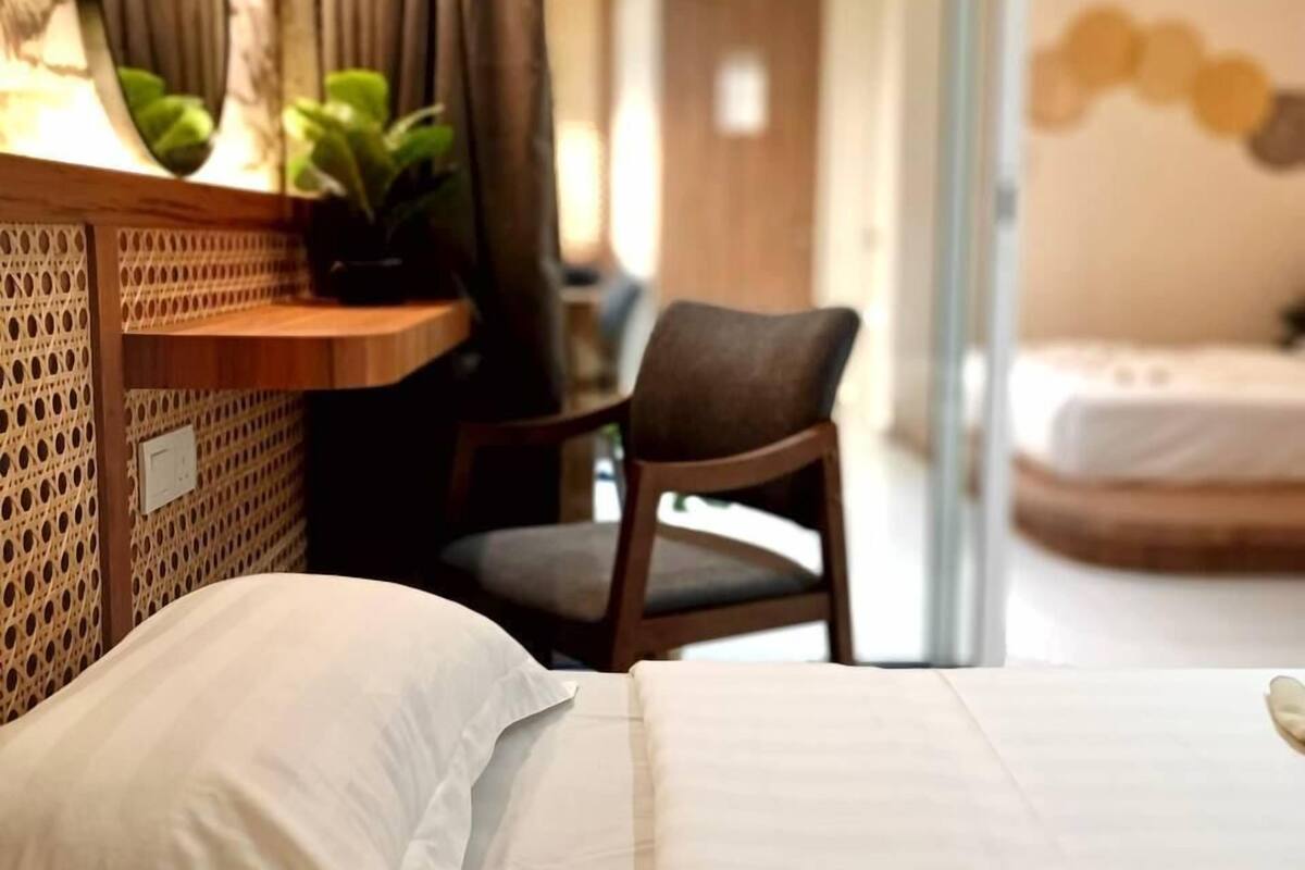 Un dormitorio con cama, una silla, un escritorio con lámpara y una pared con espejo y plantas.