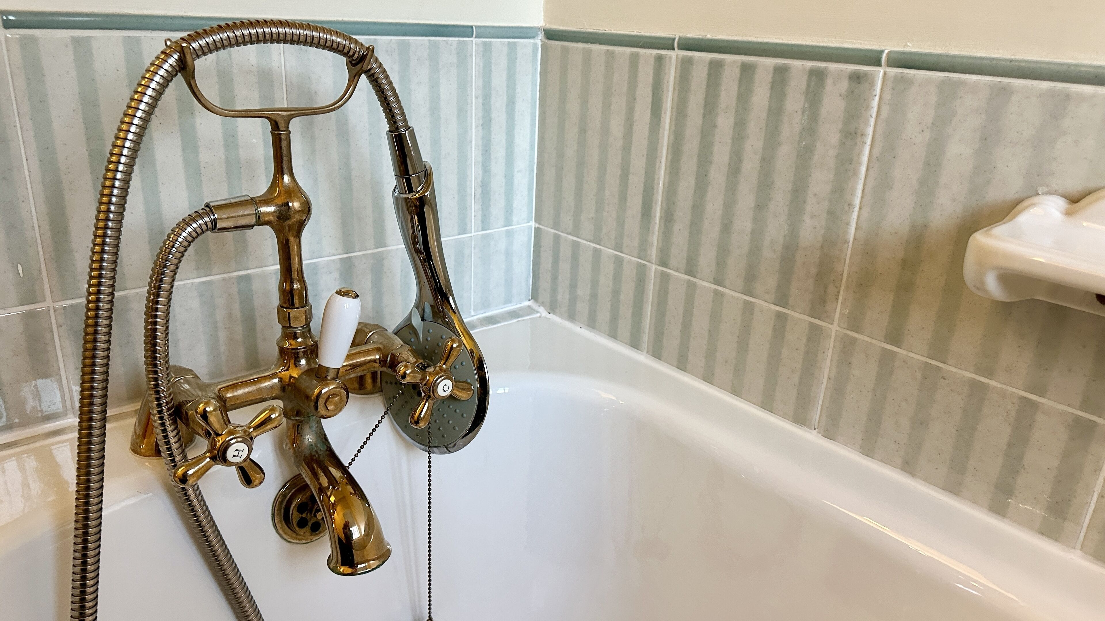 Un baño con una bañera blanca, una grifería de ducha color dorado y un jabonera blanca en la pared.