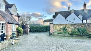 A paved driveway leading to a gated entrance with a brick wall and a hedge.