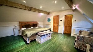 A bedroom with a wooden bed, a nightstand, a dresser, and a chair. There are two wooden doors and a radiator on the wall.