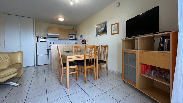A compact living space with a dining area, kitchenette, and a TV on a cabinet.