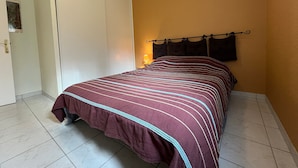 A bedroom with a bed, a door, a wall-mounted lamp, and a tiled floor.