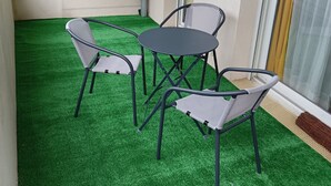 A small outdoor seating area with a round table and four chairs, surrounded by artificial green turf.