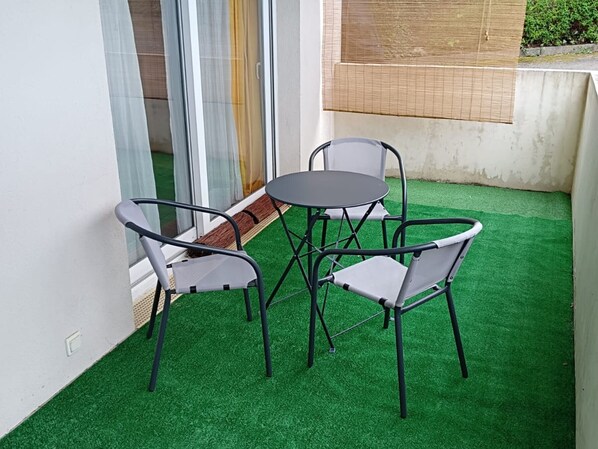 A small outdoor seating area with a round table and four chairs, surrounded by artificial green turf.