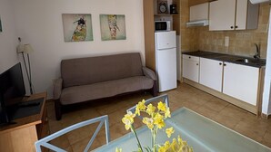 Ein gemütlicher Wohnbereich mit Sofa, Esstisch mit Blumen, Küchenzeile und Bildern an der Wand.