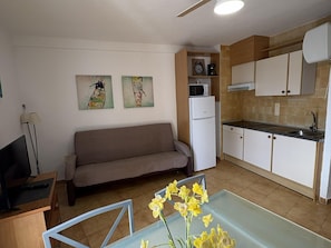 Ein gemütlicher Wohnbereich mit Sofa, Esstisch mit Blumen, Küchenzeile und Bildern an der Wand.
