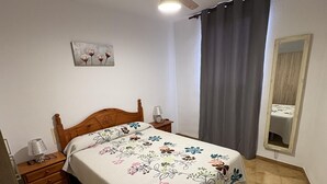 Ein Schlafzimmer mit einem hölzernen Bett, einem Nachttisch mit Lampe, einem Spiegel und einer blumigen Tagesdecke.