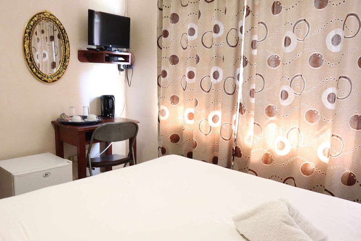 A hotel room with a bed, a desk with a chair, a television, a coffee maker, and a small refrigerator.