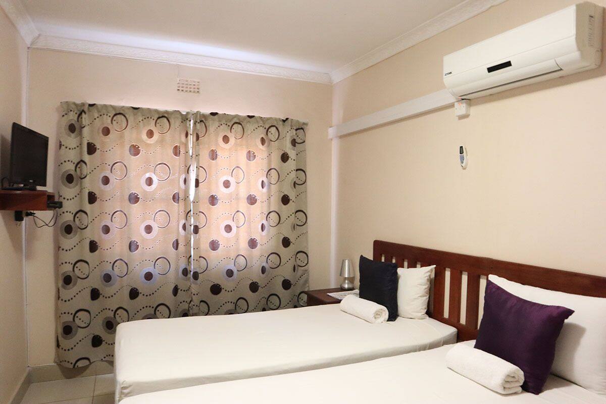 A hotel room with a bed, a TV, an air conditioner, and a curtain with a circular pattern.