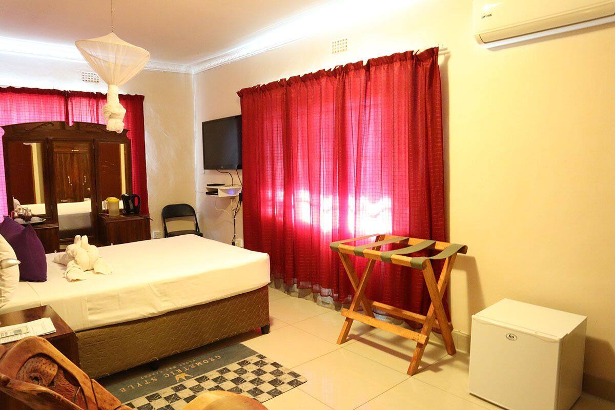 A hotel room with a bed, a desk, a chair, a TV, and a small white cabinet.