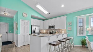 Una cocina moderna con armarios blancos, una isla central con taburetes y una pared de acento color turquesa.