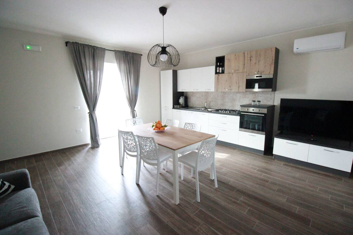 Une cuisine moderne avec des meubles blancs, une table à manger avec des chaises et un grand téléviseur à écran plat.