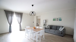 Amplia sala de estar con comedor, sofá gris y sillas blancas.