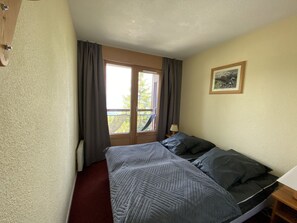 A bedroom with a bed, a window with curtains, a nightstand, a lamp, and a framed picture on the wall.