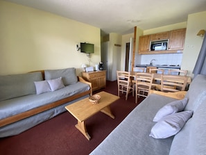 Un espacio habitable compacto con sofá, una mesa de comedor con sillas, una zona de cocina y un televisor en la pared.