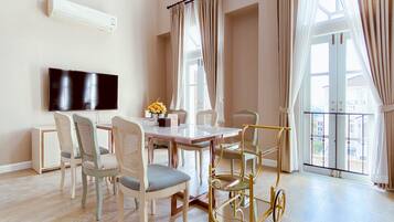 A modern dining area with a glass table, cushioned chairs, a gold-framed cart, and a flat-screen TV mounted on the wall.