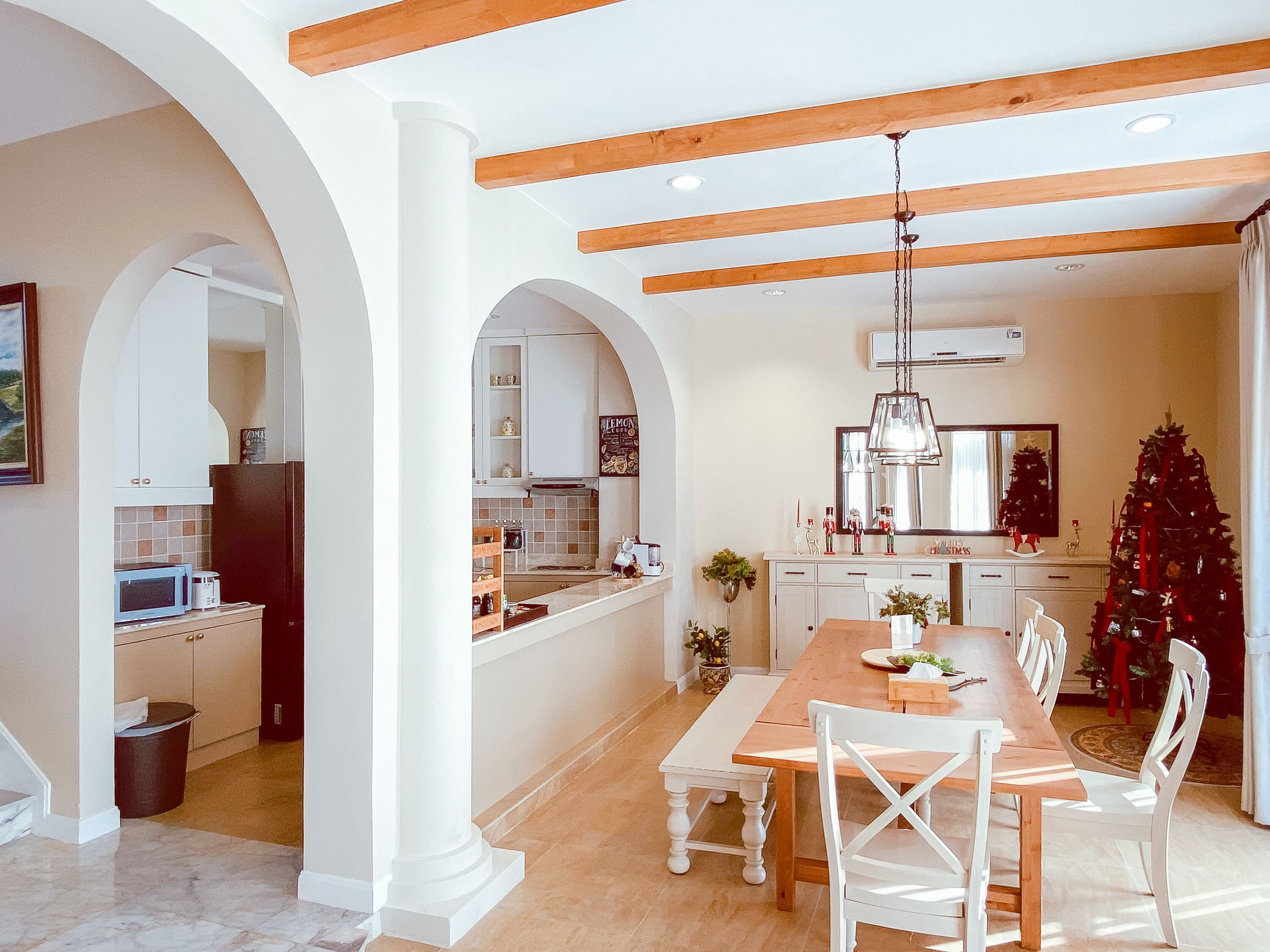 Un grand espace à manger avec une table en bois et des chaises blanches, une cuisine avec des meubles blancs et un sapin de Noël.
