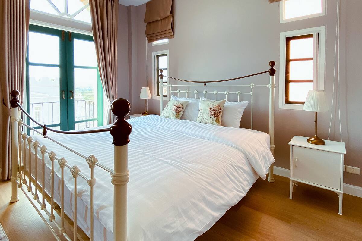 A bedroom with a bed, nightstand, lamp, and a view of the outside.