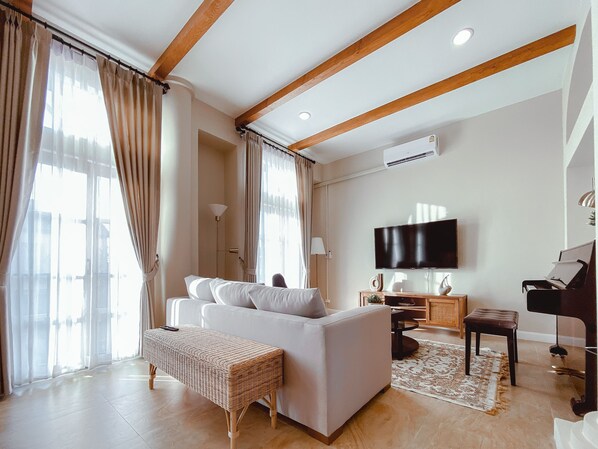 Una sala de estar moderna con un sofá blanco, un banco de mimbre, un piano y un televisor de pantalla plana.