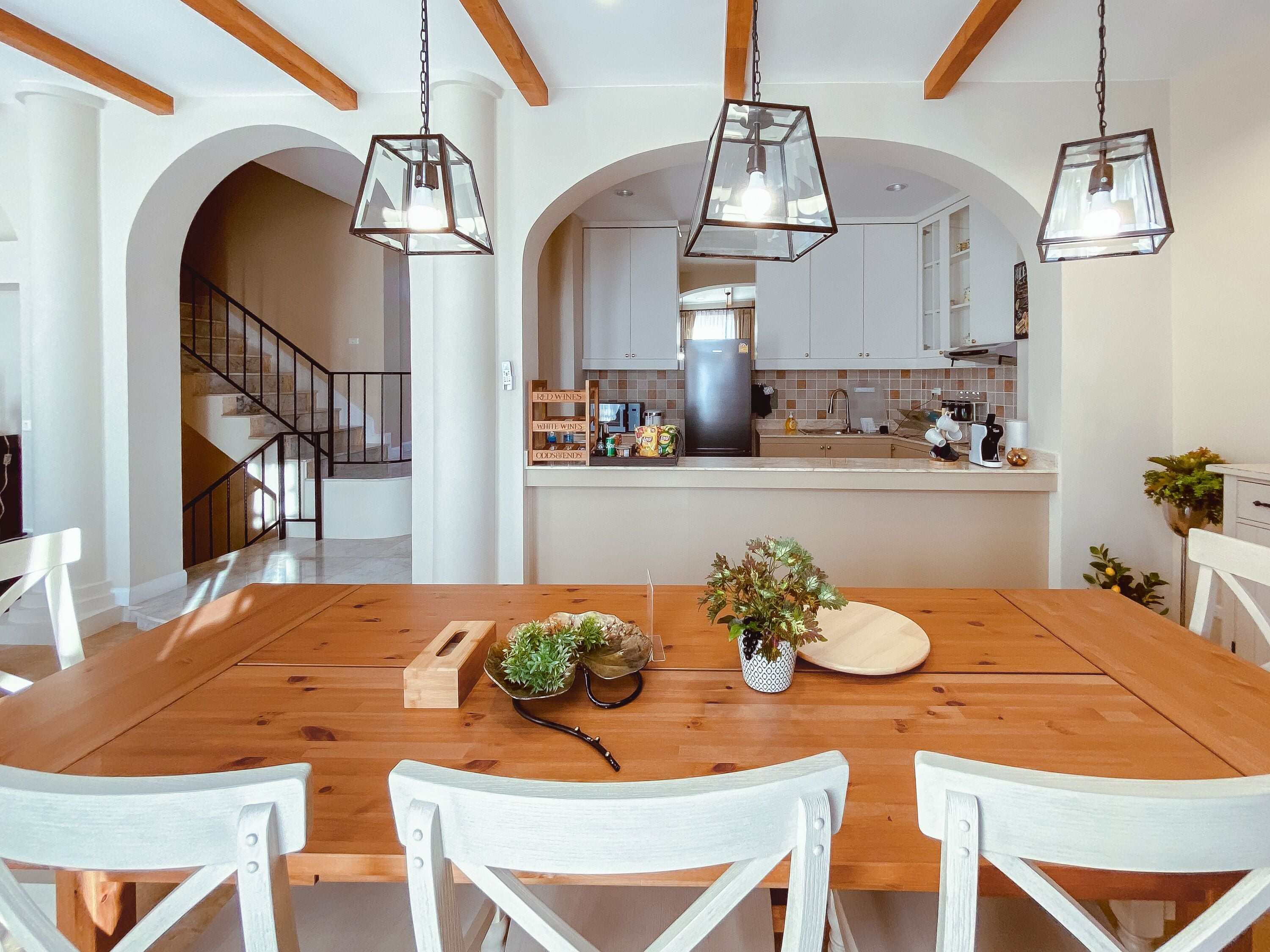 A spacious dining area with a wooden table and white chairs, featuring a central island with a plant and a decorative bowl.