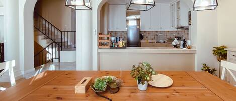 A spacious dining area with a wooden table and white chairs, featuring a central island with a plant and a decorative bowl.
