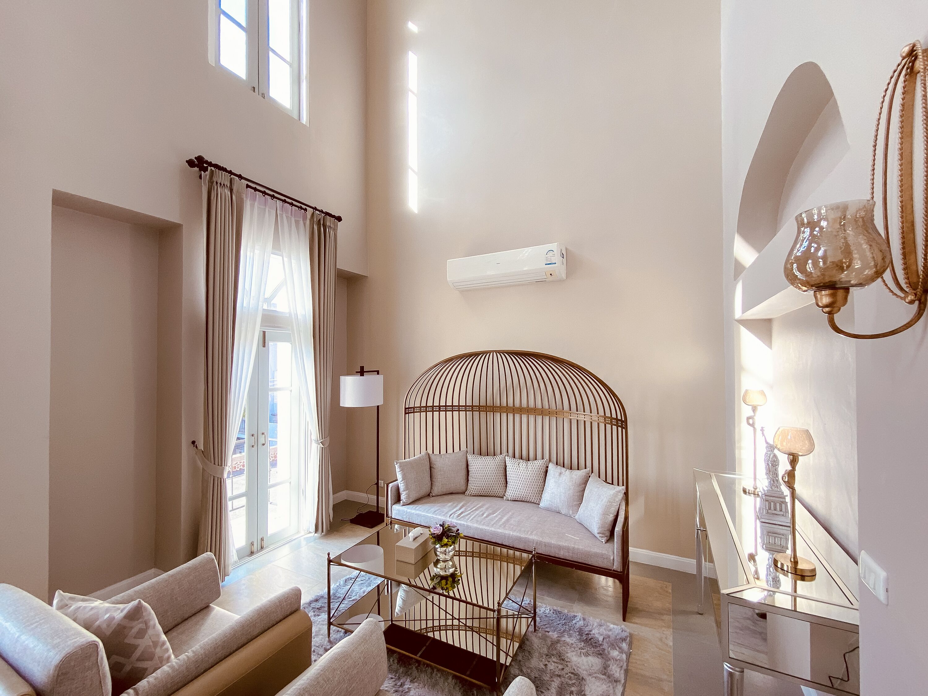 Una sala de estar moderna con un sofá, una mesa de centro de vidrio, una lámpara decorativa y un amplio ventanal con cortinas.