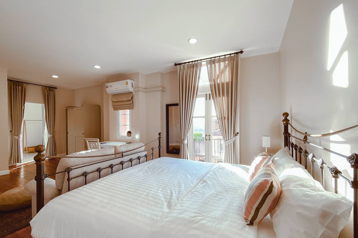 A bedroom with a large bed, a window with curtains, a mirror, and a ceiling fan.