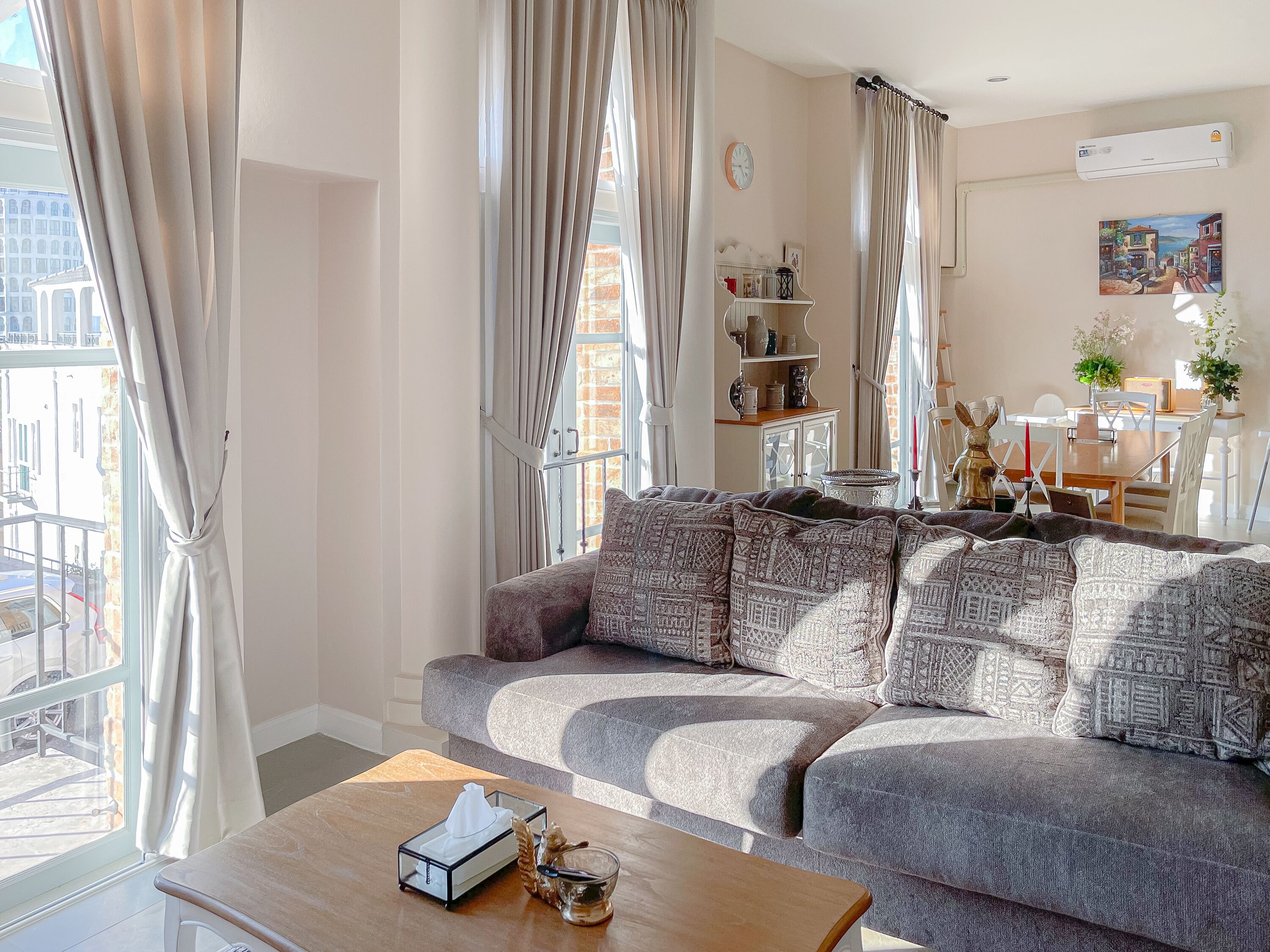 A living room with a grey sofa, a wooden coffee table, and a view of a cityscape through large windows.