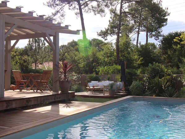 A pool area with a wooden deck, lounge chairs, and a pergola.