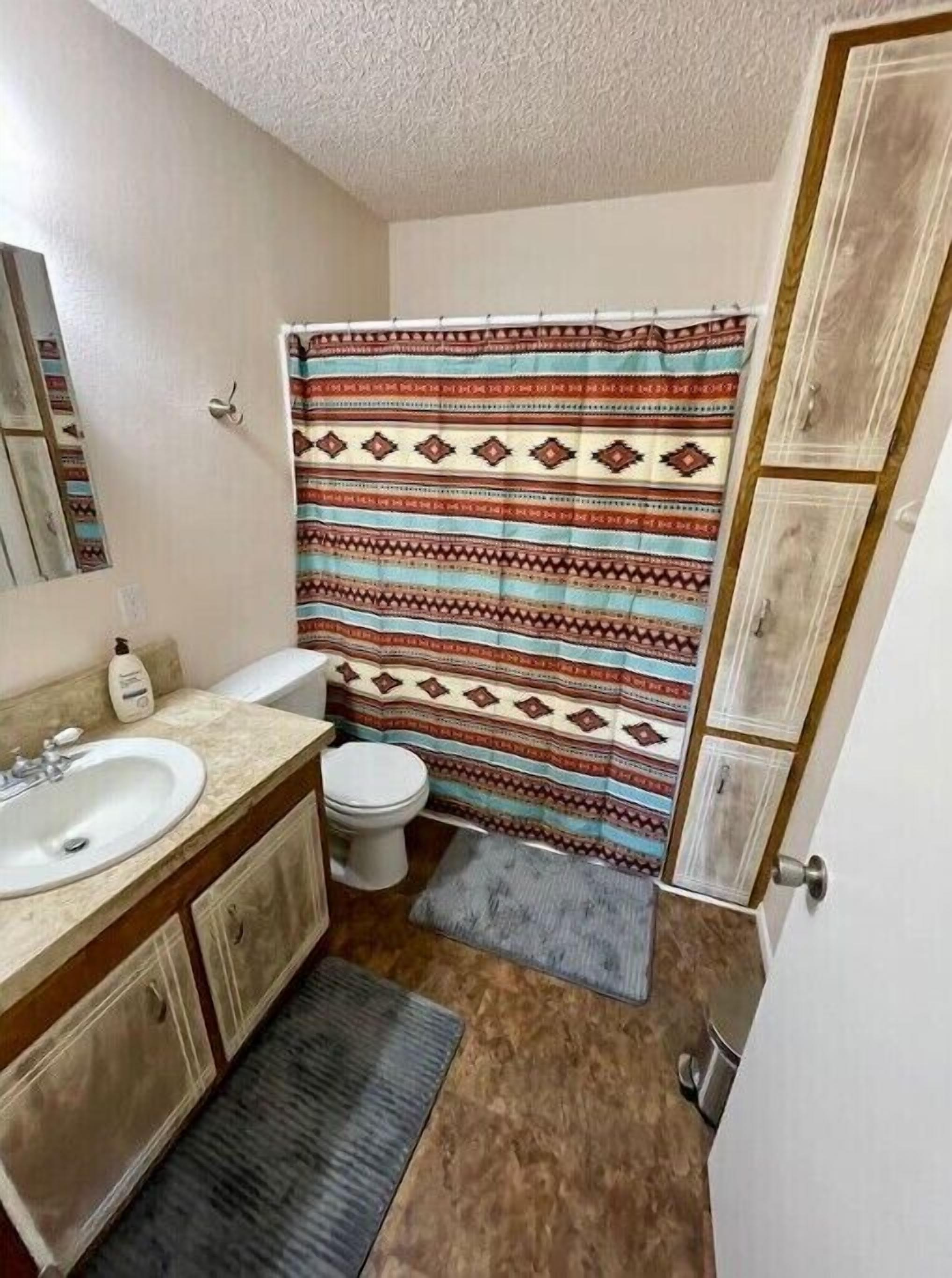 A small bathroom with a white sink, toilet, and shower curtain with a geometric pattern.
